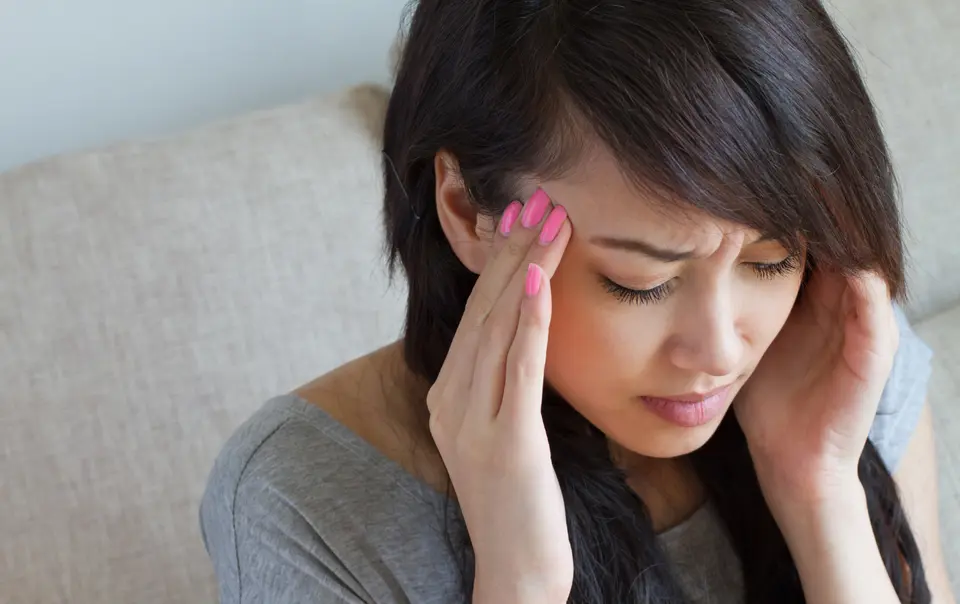 Asian woman pressing fingers against her temple